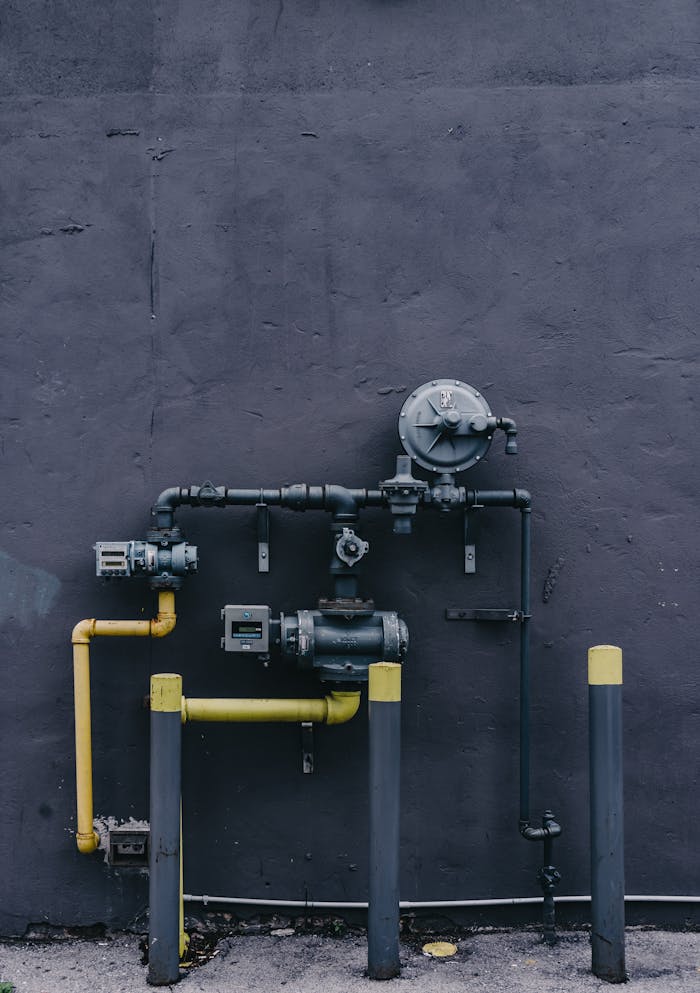 Pipes and machinery against an urban building wall with a gritty industrial look.